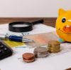 Alcancía, monedas, lupa y documento con estadísticas haciendo alusión a la tasa de interés promedio para préstamos personales