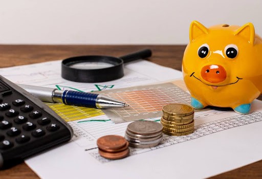 Alcancía, monedas, lupa y documento con estadísticas haciendo alusión a la tasa de interés promedio para préstamos personales